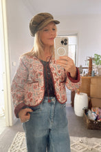 Person taking a mirror selfie wearing a boho floral jacket and jeans in a room.