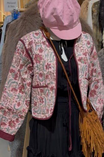 Person wearing a floral jacket and pink cap with a yellow bag in a clothing store.