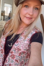 Woman wearing a brown cap and floral boho vest indoors