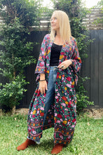 A woman standing outdoors wearing a boho kimono with a floral print, paired with a black top and blue jeans.