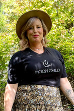 A woman wearing a black boho t-shirt with 'MOON CHILD' text, standing outdoors.