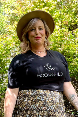 A woman wearing a black boho t-shirt with 'MOON CHILD' text, standing outdoors.