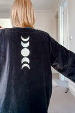 Person wearing a black jacket with white moon phase design on the back, standing indoors.