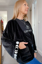 Person wearing a black jacket with white patterns and text, standing indoors.