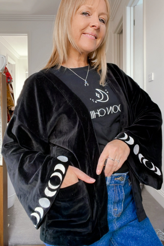 A person wearing a black boho velvet jacket with moon phase embroidery, paired with blue jeans.