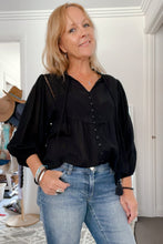 Woman wearing a black boho blouse and blue jeans indoors.