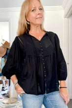 Woman wearing a black boho blouse and blue jeans indoors.