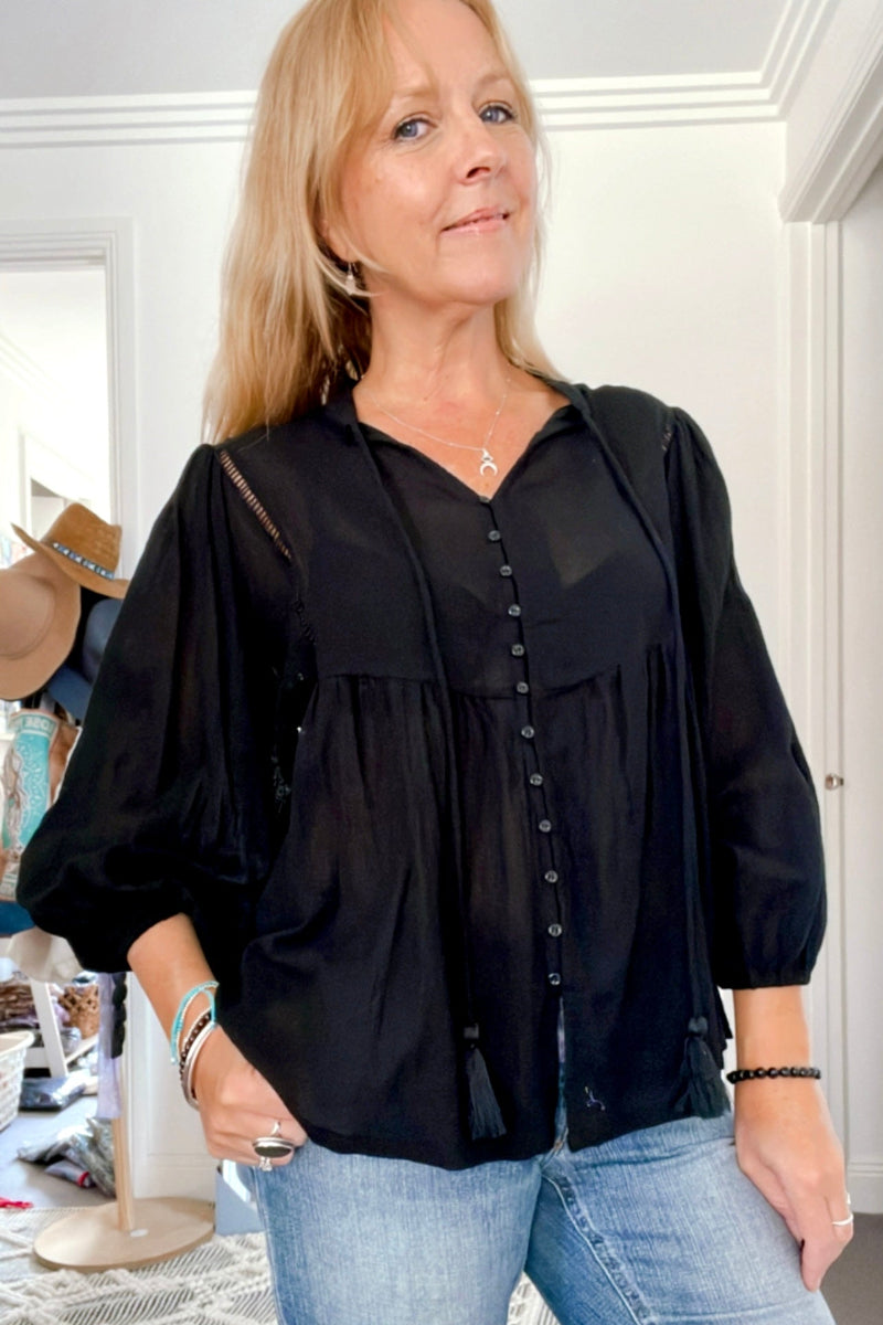 Woman wearing a black boho blouse and blue jeans indoors.