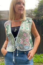 A woman wearing a green boho patchwork cotton vest with a square cut and front tie, paired with blue jeans.