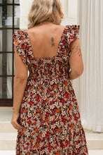 Woman wearing a boho floral dress with tattoos visible on her arms, standing in front of classical architecture.