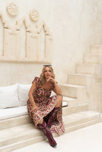 Woman in a floral dress and boots sitting on a staircase with decorative wall behind