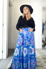 Woman wearing a black top and blue floral boho skirt indoors.