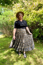 Woman wearing a black t-shirt with 'Moonchild' text and a bohemian floral skirt standing in a garden.
