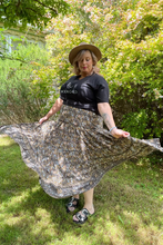 Woman in a floral boho skirt and black t-shirt standing outdoors with trees in the background