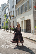 Woman in a long black boho dress walking down a street in a European city.