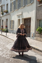 Woman in a black floral boho dress walking down a cobbled street in a European town.