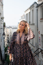 Woman in a floral boho dress standing on a city street with buildings in the background