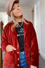 Person wearing a red velvet boho coat, black t-shirt, and blue jeans indoors.