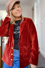 Person wearing a red velvet boho jacket over a black shirt with white text, standing indoors.