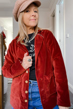 Person wearing a red velvet jacket, beige cap, and blue jeans indoors.