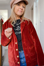 Person wearing a boho red jacket, black t-shirt, and blue jeans indoors.