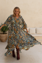 Woman in a floral boho dress and red boots standing in a living room.