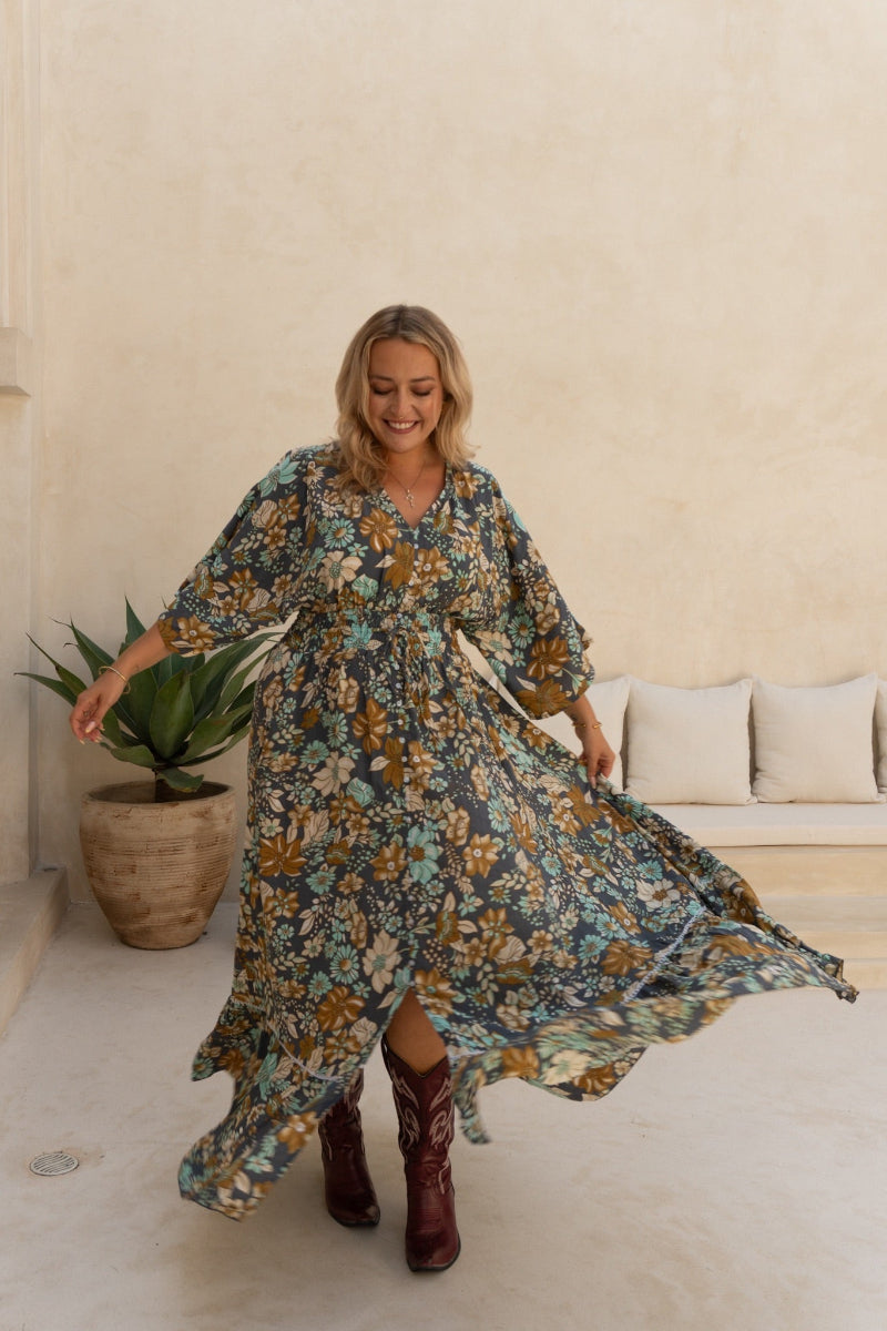 Woman in a floral boho dress standing in a room with a plant and sofa.