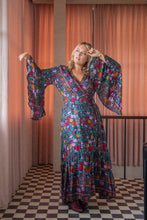 Woman wearing a colorful floral dress in a room with orange curtains and checkered floor.