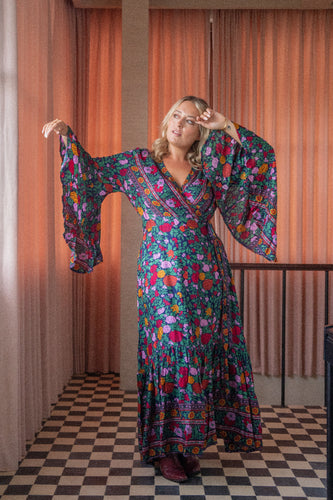 Woman wearing a colorful floral dress in a room with orange curtains and checkered floor.