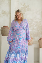 Woman wearing a purple and blue floral boho dress standing in a room with decorative vases.