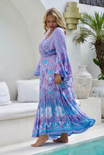 Woman in a long, boho patterned dress standing by a poolside.