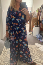 Person wearing a blue patterned jumpsuit taking a mirror selfie in a room.