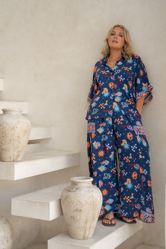 A person standing on a staircase wearing navy wide leg pants with a tequila print and a matching blouse.