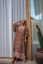 A woman wearing a bohemian floral maxi dress stading beside the door.