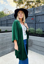 A woman wearing the Eclectic Bohemian Emerald Mystic Moth Velvet Jacket in emerald green, featuring a large gold-embroidered moth on the side view.