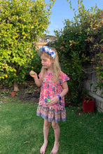 Young girl in a colorful dress standing in a garden holding small objects.