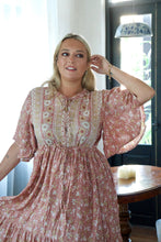 Woman wearing a floral dress in a room with a table and window.
