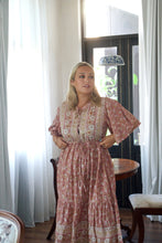 Woman wearing a floral dress standing in a room with curtains and a table.