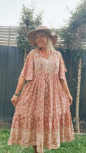 A Woman wearing a floral boho dress and a hat, standing outside the garden.
