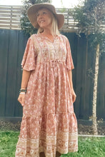 Woman wearing a patterned dress and hat standing outdoors.