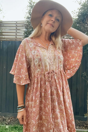 Woman wearing a boho floral dress and wide-brimmed hat outdoors.