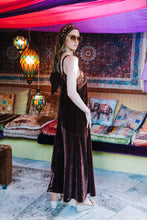 Woman in a long dark boho dress standing in a colorful room with patterned rugs and hanging lights.