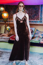 Woman wearing a dark brown velvet boho dress with floral lace details in a colorful, patterned room.