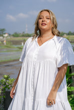 Woman in a white boho dress standing outdoors with a scenic background