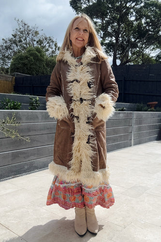 Woman wearing a brown boho coat with white fur trim and a colorful dress, standing outdoors.