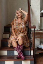 Woman in a boho patterned dress and cowboy boots sitting on wooden stairs.