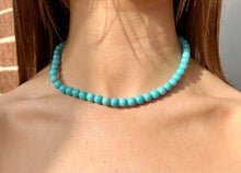 A person wearing a turquoise beaded necklace with an adjustable chain.