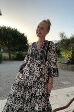 Woman in a black and white patterned dress standing outdoors with trees and a clear sky in the background.