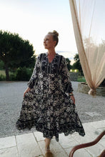 Woman in a floral dress standing outdoors with trees and a draped fabric in the background