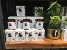 Asana Candle products displayed on a wooden shelf with plants in the background